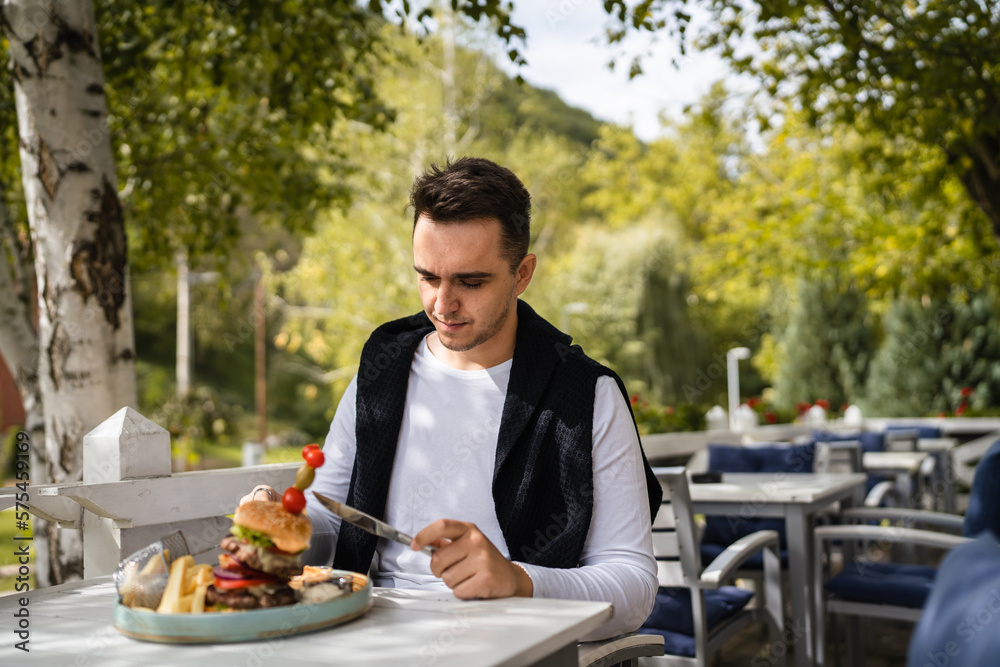 one young man sit at table eat burger and chips at restaurant outdoor one young man sit at table eat burger and chips at restaurant outdoor