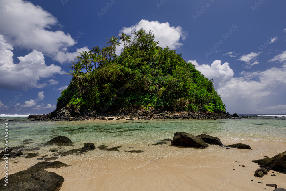 Amanave Bay coastline with blue sky and white clouds showing the sandy beach and black lava boulders 