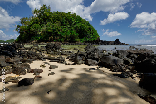 Amanave Bay coastline with blue sky and white clouds showing the sandy beach and black lava rocks 