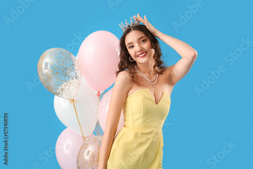 Beautiful young woman in prom dress and with balloons on blue background