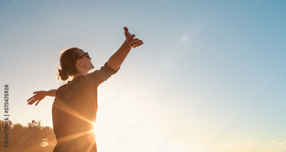 woman enjoying the sun feeling joyful with open arms  - obrazy, fototapety, plakaty 