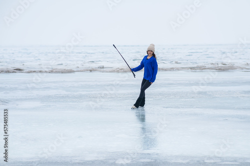 A caucasian woman is skating on a frozen lake holding a selfie stick in her hands. The figure skater films her skating.