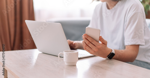 Lady with smartphone working at laptop at table and cup of coffee.