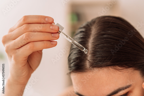 Lady dripping hair oil with pipette on her hair.