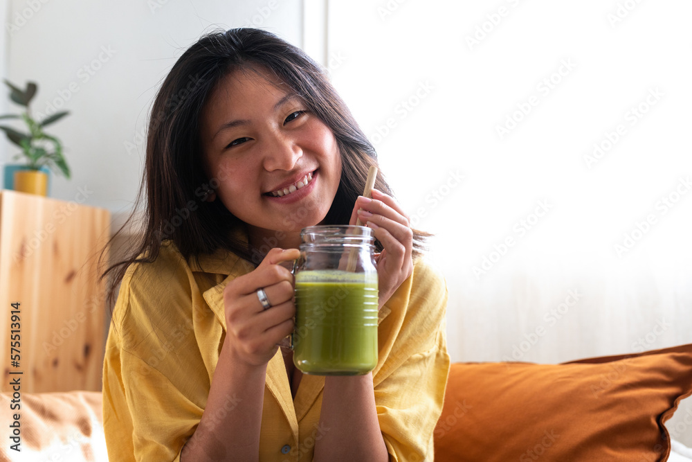 Happy teen asian girl showing healthy green juice looking at camera. Copy space. Copy space. Happy teen asian girl showing healthy green juice looking at camera. Copy space. Copy space.