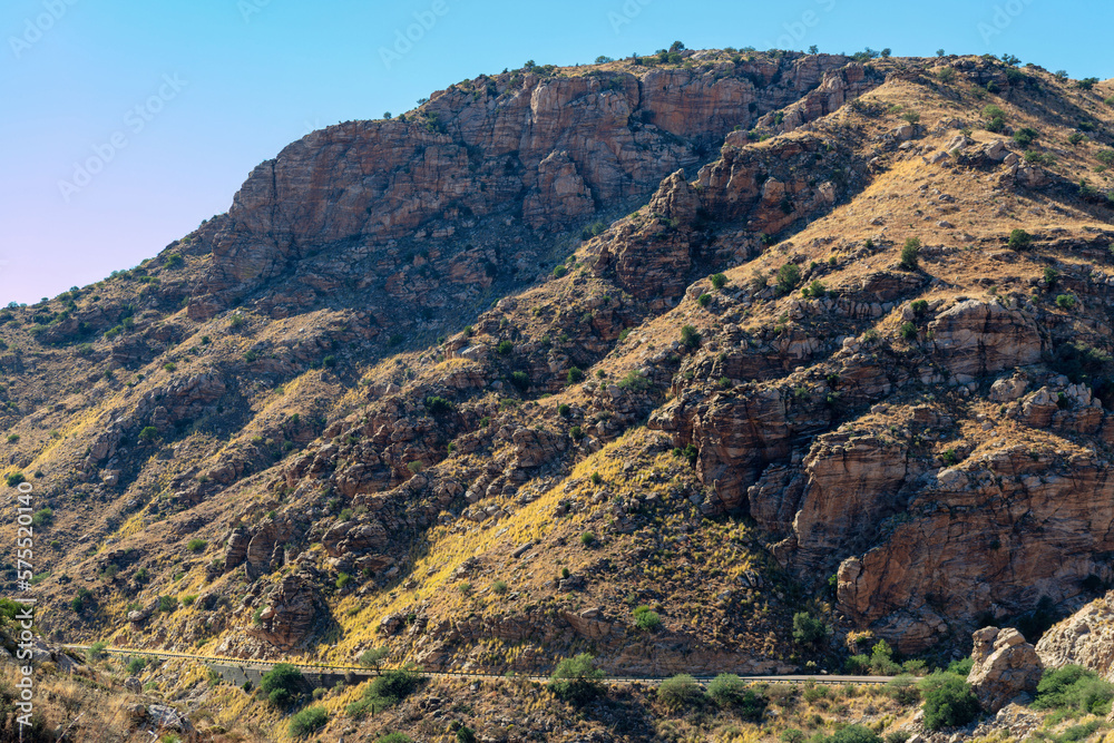 Giant mountain with small visible road near base with cars and pedestrians in the great outdoors in arizona midday sun