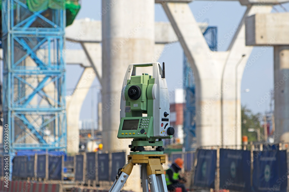 Construction level, surveyor engineer with equipment (theodolite or total station) at the construction site of a road or building with construction machinery