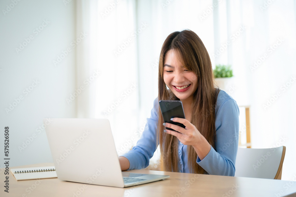 Young asian woman working on computer laptop and hand typing chat on mobile smartphone at home Young asian woman working on computer laptop and hand typing chat on mobile smartphone at home