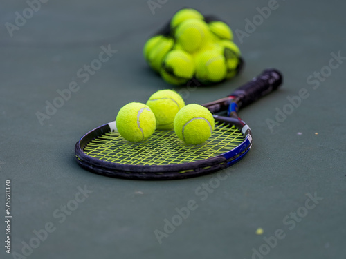 raqueta de tenis en el suelo de la cancha con bolas encima y grupo de pelotas detrás 
