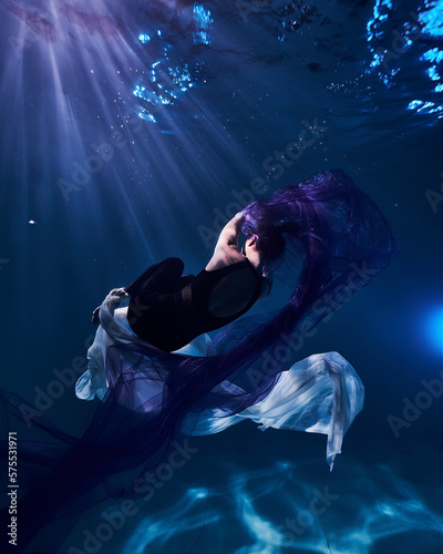 a young beautiful girl is swimming in a pool under water fashion fabric on a dark blue background like in the sea