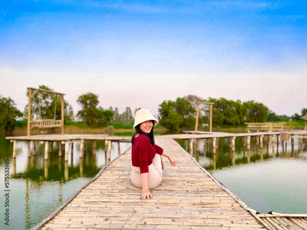 Fototapeta premium Young girl enjoying beauty of nature looking at lake. Adventure travel of woman sits on wooden bridge.
