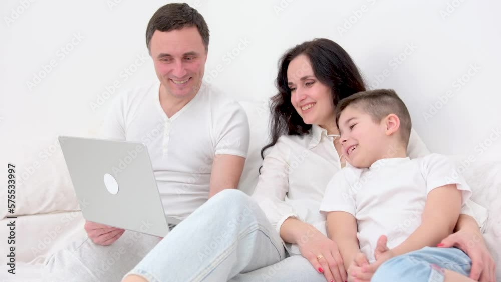 family in bed playing on tablet sincerely laughing having fun mom father and son dark hair white big duvet family is watching movies with the son on laptop good way to spend time on quarantine. family in bed playing on tablet sincerely laughing having fun mom father and son dark hair white big duvet family is watching movies with the son on laptop good way to spend time on quarantine.