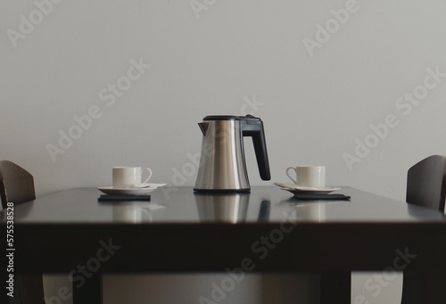 two white cups and a coffee pot on a black wooden table and two chairs