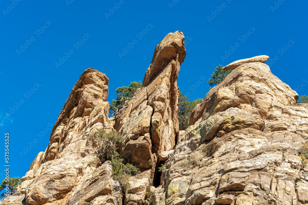 Rocky cliffs in the afternoon sun with hanging stones on natural rock formation with clear blue sky background