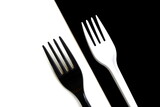 A white fork lies on a black background and a black fork lies on a white background.