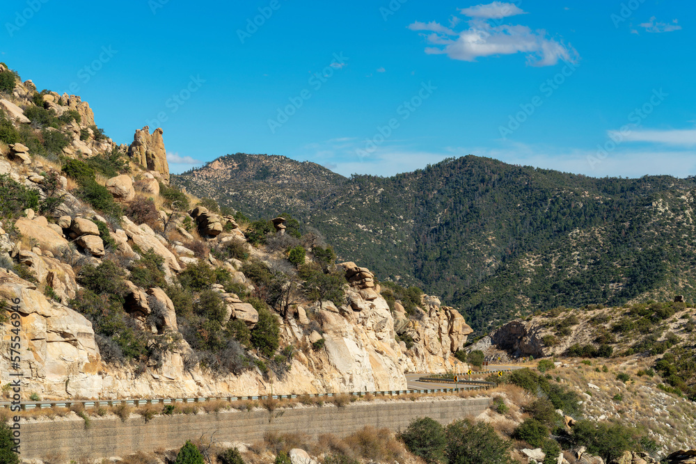 Mountain road in the afternoon sun with blue sky and few clouds with rock and stone formations on side of cliff