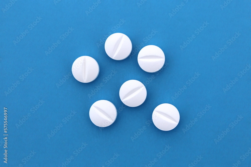 A pile of white pills lie on a blue background. A pile of white pills lie on a blue background.