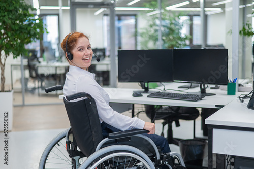 Red-haired caucasian woman in a wheelchair talking on a headset. Female call center worker smiling.