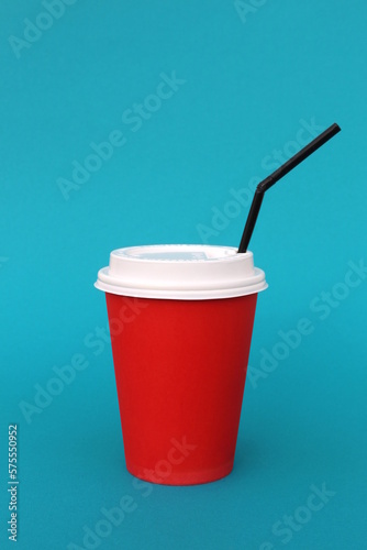 A bright disposable paper cup for coffee stands on a turquoise background.