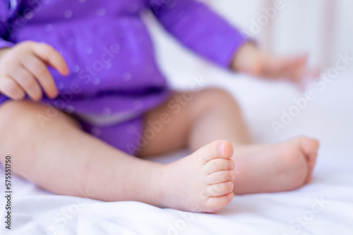 the legs or feet of a small newborn baby on a white cotton bed at home in a crib, pink baby heels © Any Grant