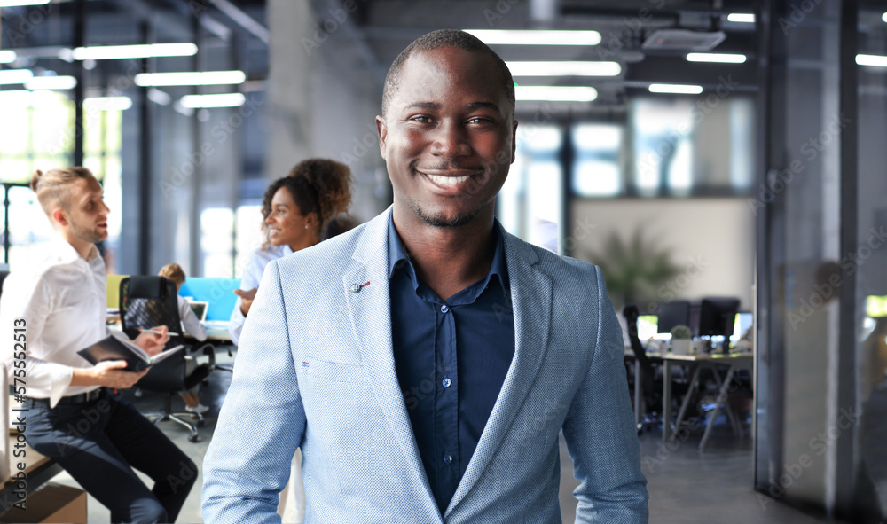 Portrait of smiling African American business man with executives working in background Portrait of smiling African American business man with executives working in background