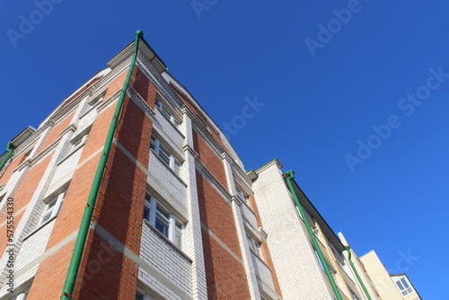  high-rise multi-storey brick house stands against a blue sky, photo from bottom to top.