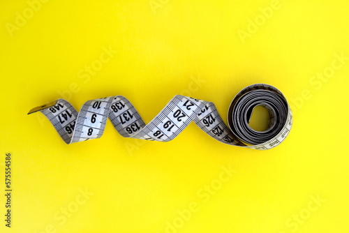 A twisted centimeter tape lies on a yellow background photo