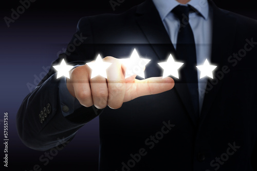 Quality rating. Man pressing on star on virtual screen against dark background, closeup