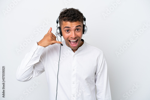 Telemarketer Brazilian man working with a headset isolated on white background making phone gesture. Call me back sign