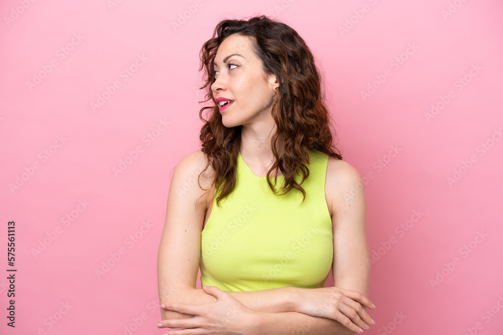Young caucasian woman isolated on pink background looking to the side