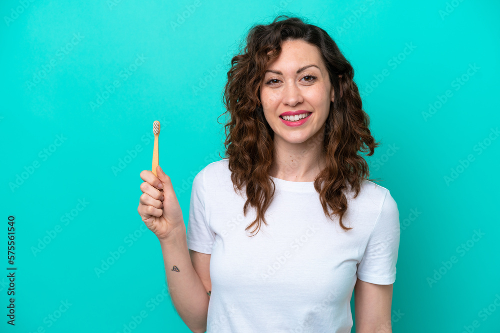 Young caucasian woman brushing teeth isolated on blue background smiling a lot Young caucasian woman brushing teeth isolated on blue background smiling a lot