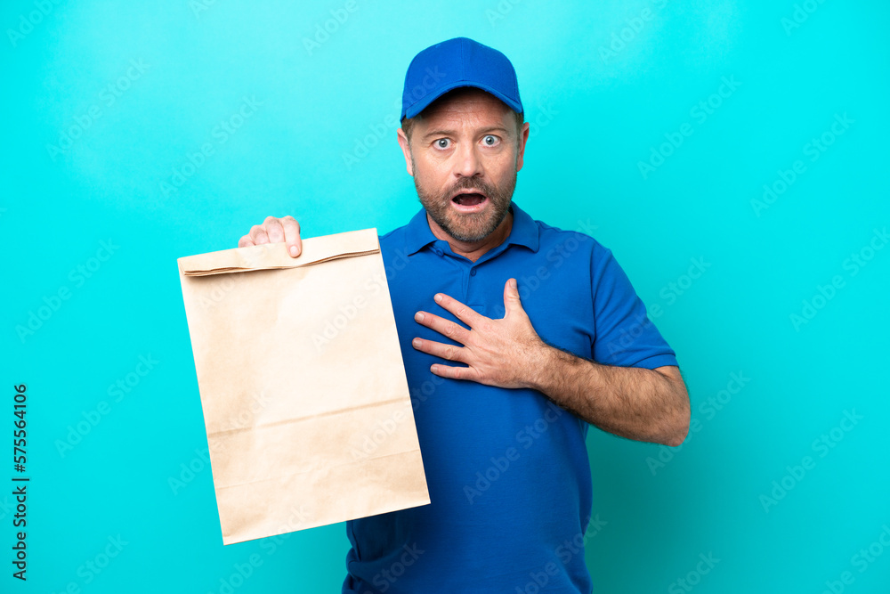 Middle age man taking a bag of takeaway food isolated on blue background surprised and shocked while looking right Middle age man taking a bag of takeaway food isolated on blue background surprised and shocked while looking right