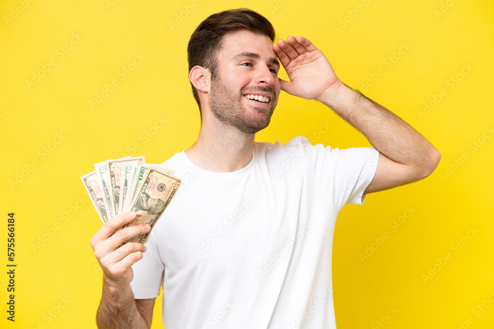 Young caucasian man taking a lot of money isolated on yellow background smiling a lot Young caucasian man taking a lot of money isolated on yellow background smiling a lot