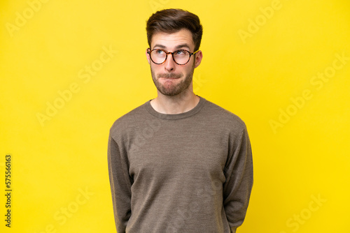 Young caucasian man isolated on yellow background having doubts while looking up
