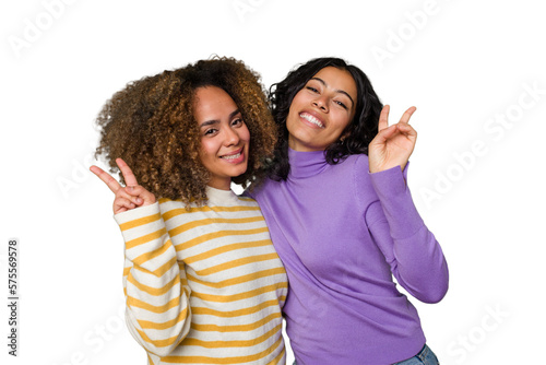 Fotografie Two female friends isolated in studio joyful and carefree showing a peace symbol with fingers