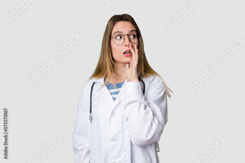 Compassionate female physician with a stethoscope around her neck  ready to diagnose and care for her patients in her signature white coat is saying a secret hot braking news and looking aside