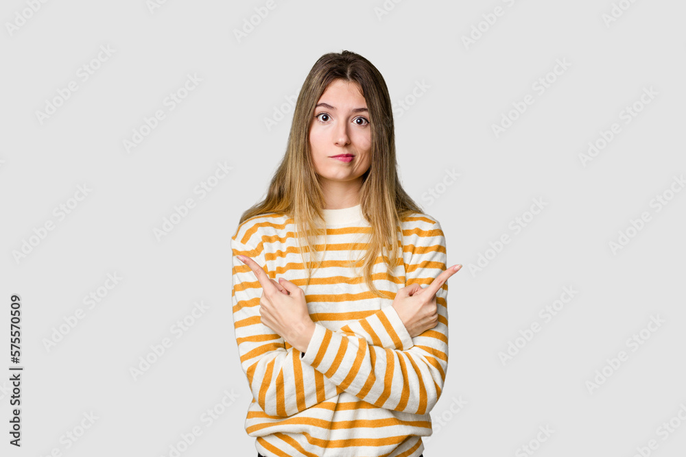 Young blonde posing for a portrait isolated, exuding natural beauty and radiance points sideways, is trying to choose between two options. Young blonde posing for a portrait isolated, exuding natural beauty and radiance points sideways, is trying to choose between two options.