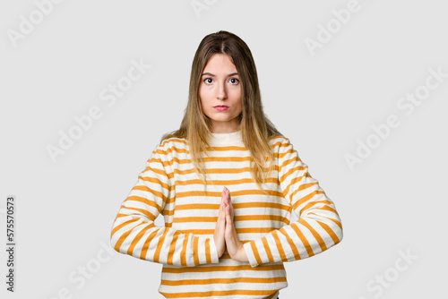 Young blonde posing for a portrait isolated, exuding natural beauty and radiance praying, showing devotion, religious person looking for divine inspiration. © Asier