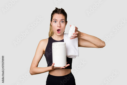 Young woman holding a container of protein powder, dressed in sportswear, focused on her fitness routine photo