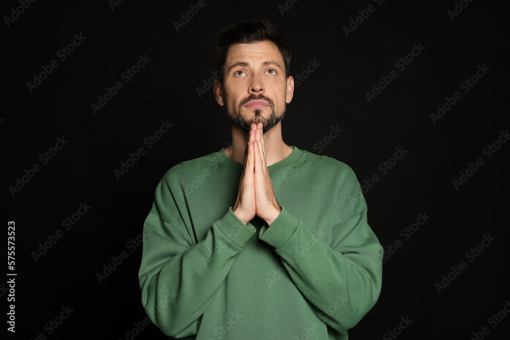 Man with clasped hands praying on black background Man with clasped hands praying on black background