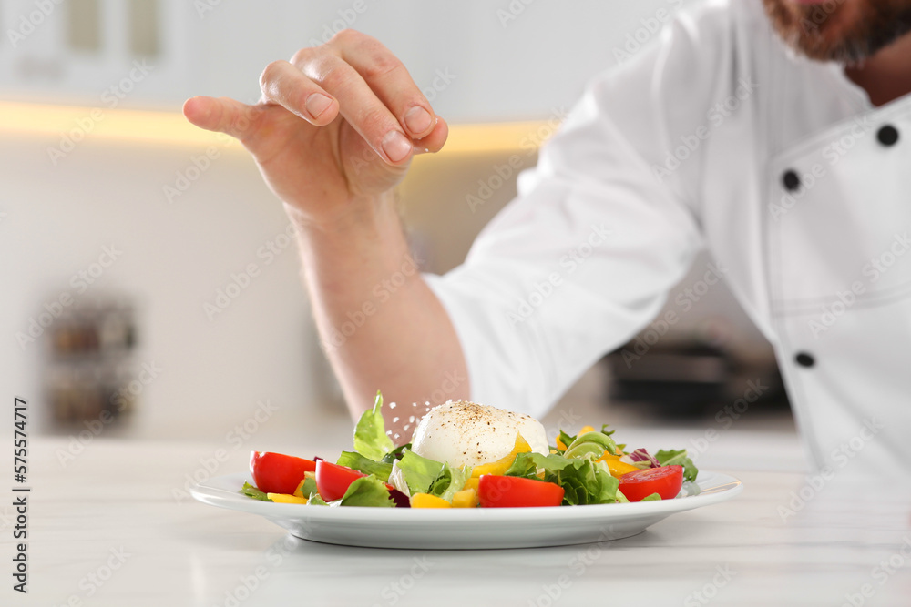 Professional chef salting delicious salad at marble table, closeup