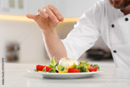 Professional chef salting delicious salad at marble table  closeup