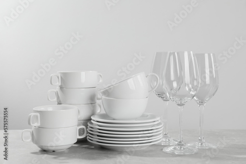 Set of clean dishware and glasses on grey table against light background
