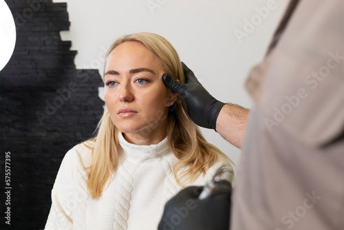 Doctor pulls female facial skin, lifting temple area, preparing to face reshape with filler, injection, surgery. Beauty physician, surgeon, woman are in examination room.Aesthetic medicine. Horizontal