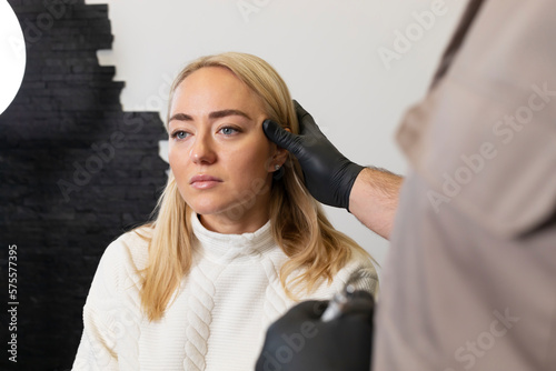 Doctor pulls female facial skin, lifting temple area, preparing to face reshape with filler, injection, surgery. Beauty physician, surgeon, woman are in examination room.Aesthetic medicine. Horizontal photo