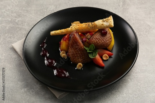 Plate with delicious chicken, parsnip and strawberries on grey table. Food stylist