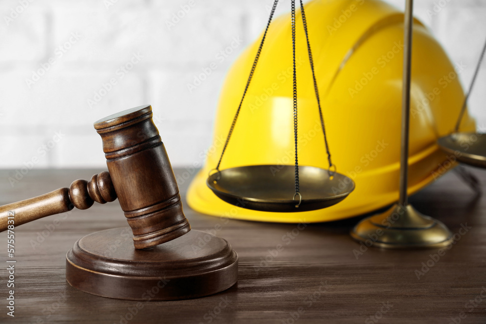 Labour, construction and land law concepts. Judge gavel, scales of justice with protective helmet on wooden table Labour, construction and land law concepts. Judge gavel, scales of justice with protective helmet on wooden table