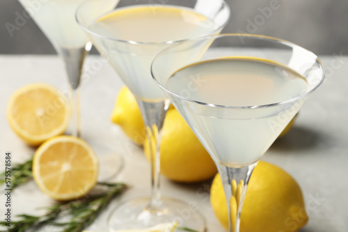 Martini glasses of refreshing cocktail, lemon and rosemary on light grey table, closeup