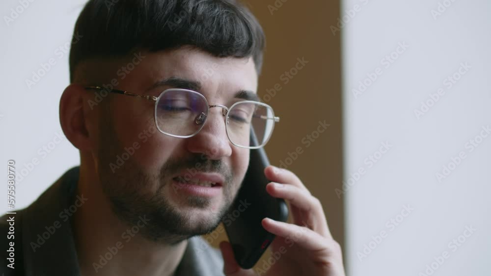 Businessman starts laughing during a telephone conversation. Discussing work tasks over the phone. Young man in glasses answering call with smile Businessman starts laughing during a telephone conversation. Discussing work tasks over the phone. Young man in glasses answering call with smile