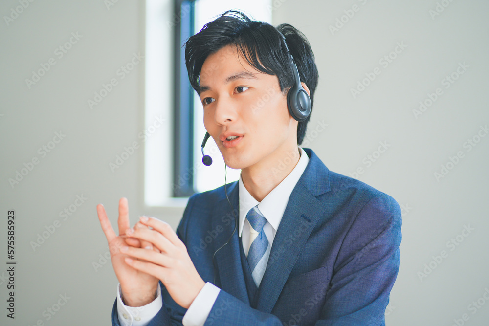 ヘッドセットをつけてインサイドセールスをするスーツ姿の若い男性 ヘッドセットをつけてインサイドセールスをするスーツ姿の若い男性